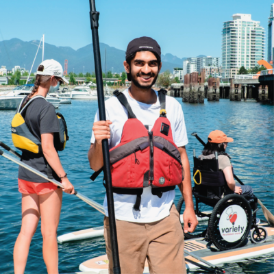 Sahil standing on BCMOS Paddling dock, wearing a life jacket and holding a paddle.