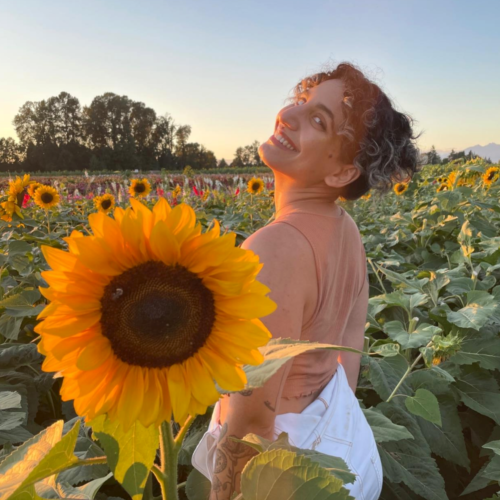 Nousha Bayrami smiling and posing outdoors in a sunflower field.