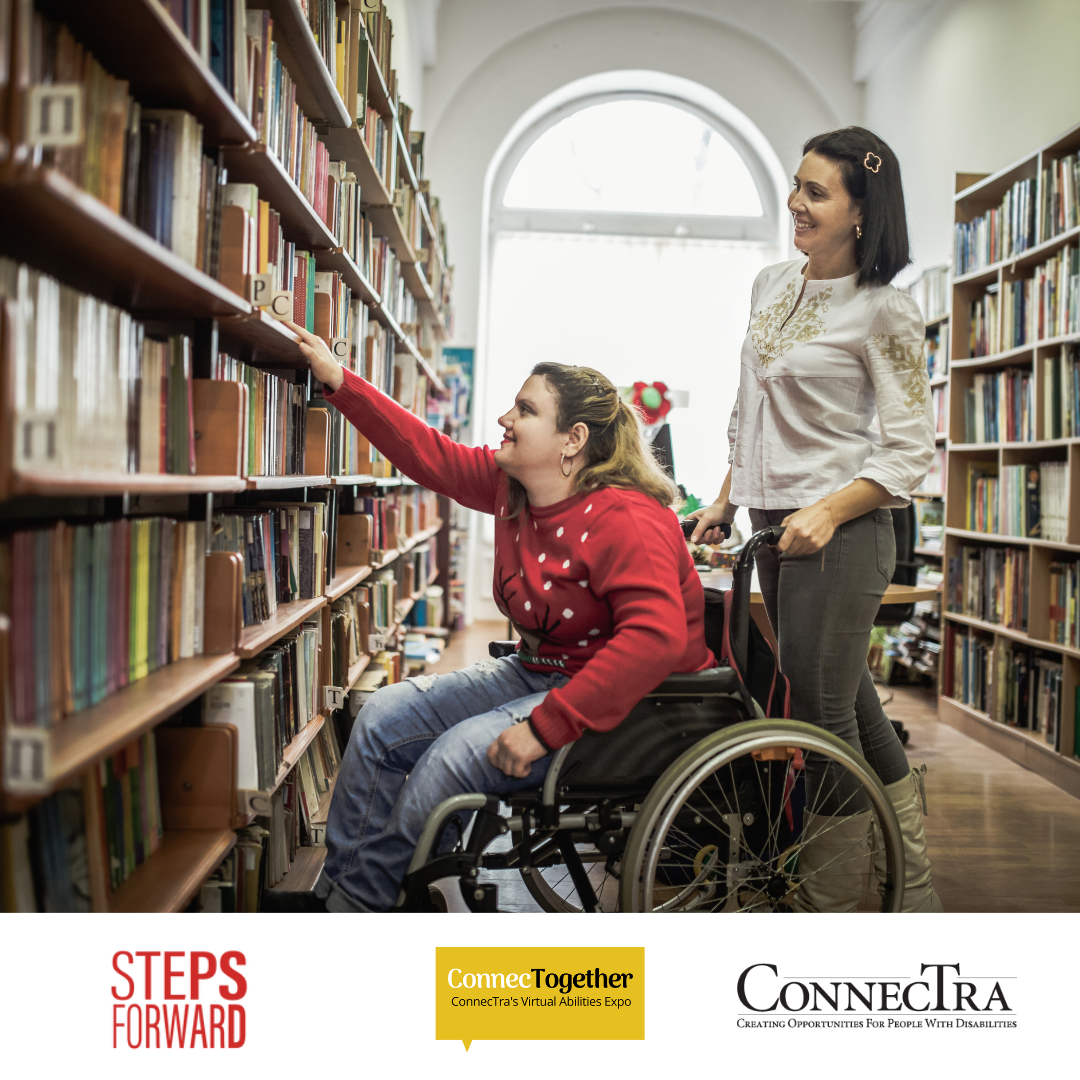 Individual in wheelchair reaches for a book out of a bookshelf, while another person stands just behind her.